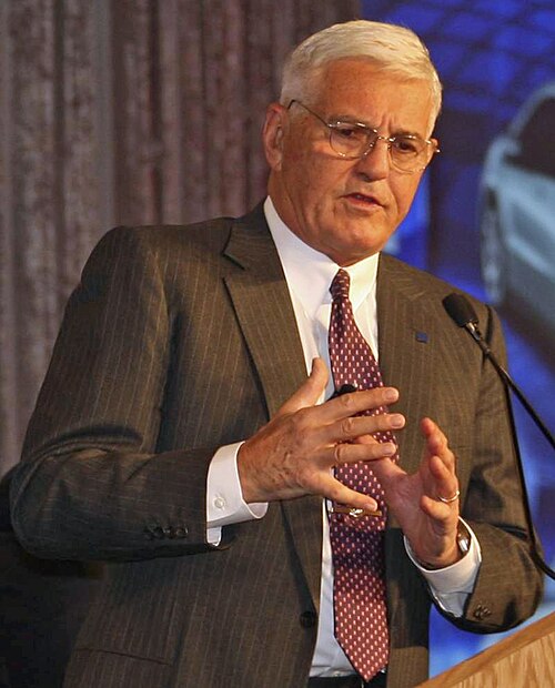 A man presumed to be Robert "Bob" Lutz speaking at a podium, October 2008